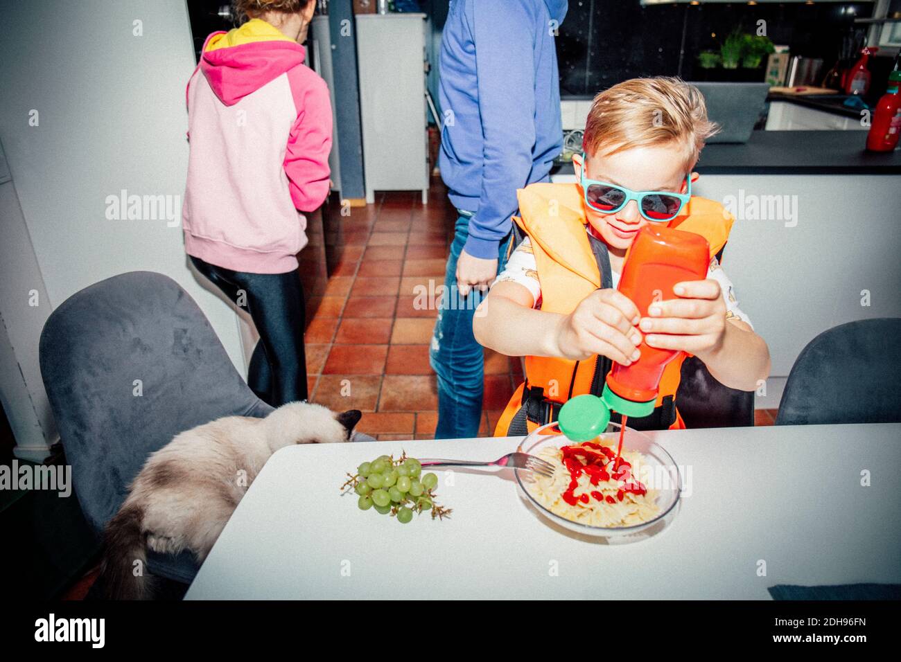 Ragazzo che versa il ketchup al tavolo di mattina Foto Stock