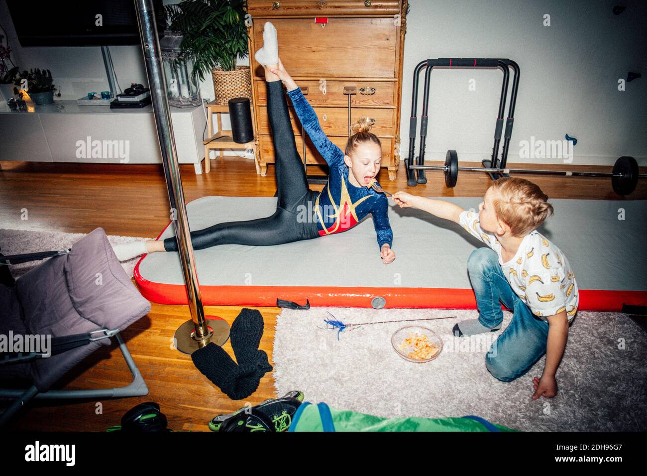 Ragazza che pratica mentre fratello che alimenta sorella in soggiorno Foto Stock