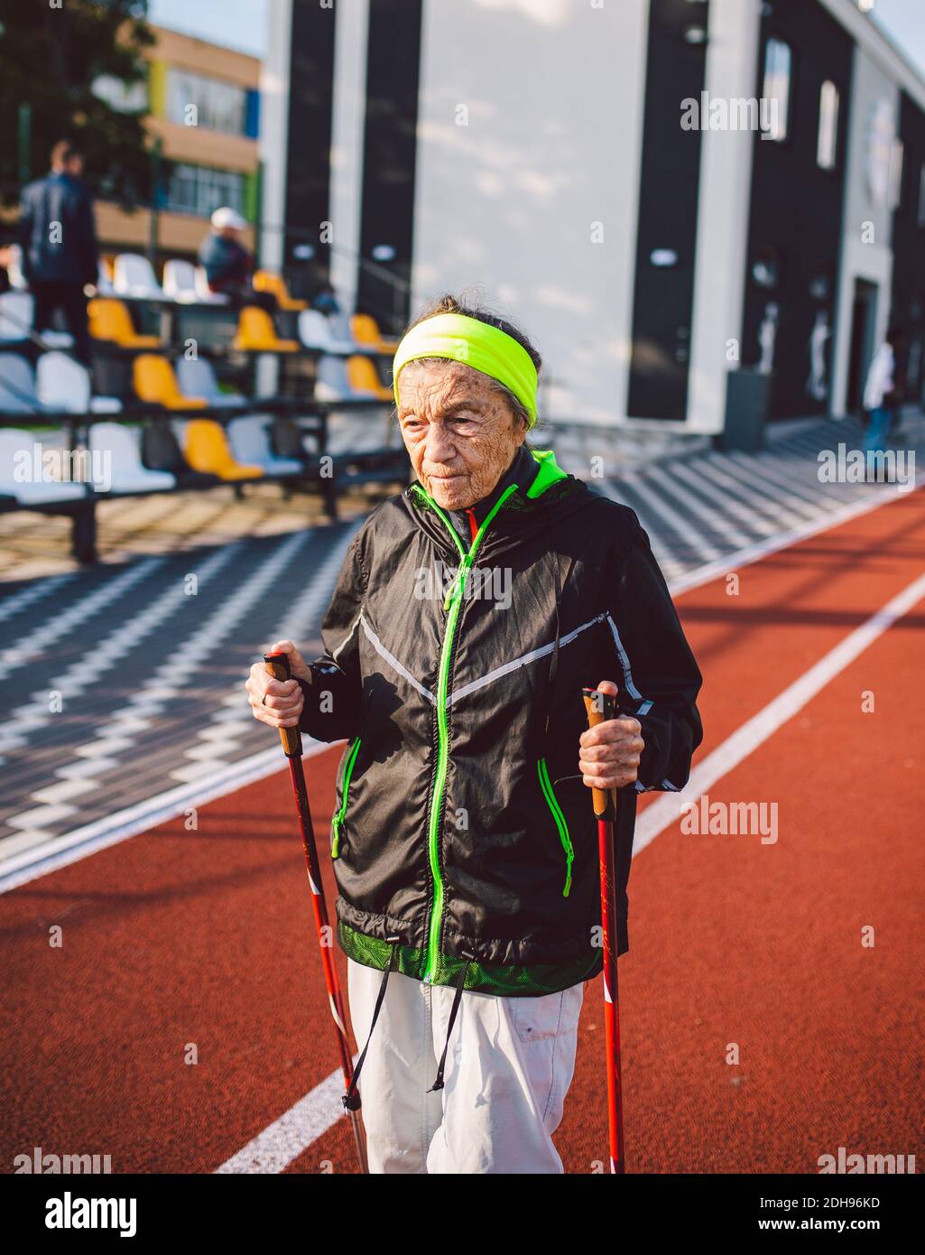 Donna anziana in abbigliamento sportivo che pratica nordic walking  all'aperto su tapis roulant in gomma nello stadio. Più anziana passeggiata  femminile di scandinavian wal Foto stock - Alamy