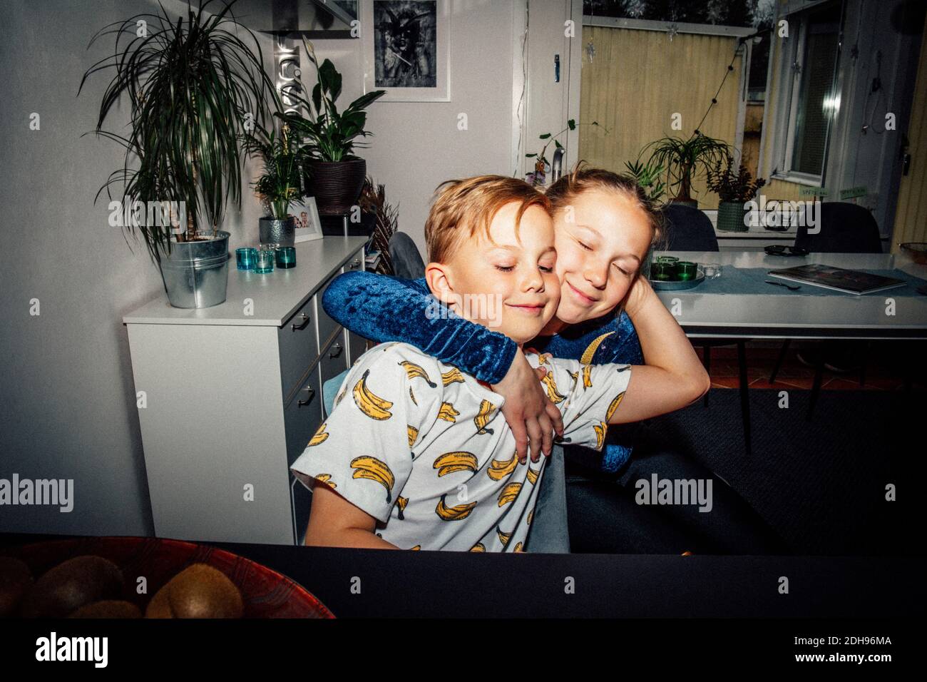 Ragazza sorridente che abbraccia il fratello in soggiorno Foto Stock