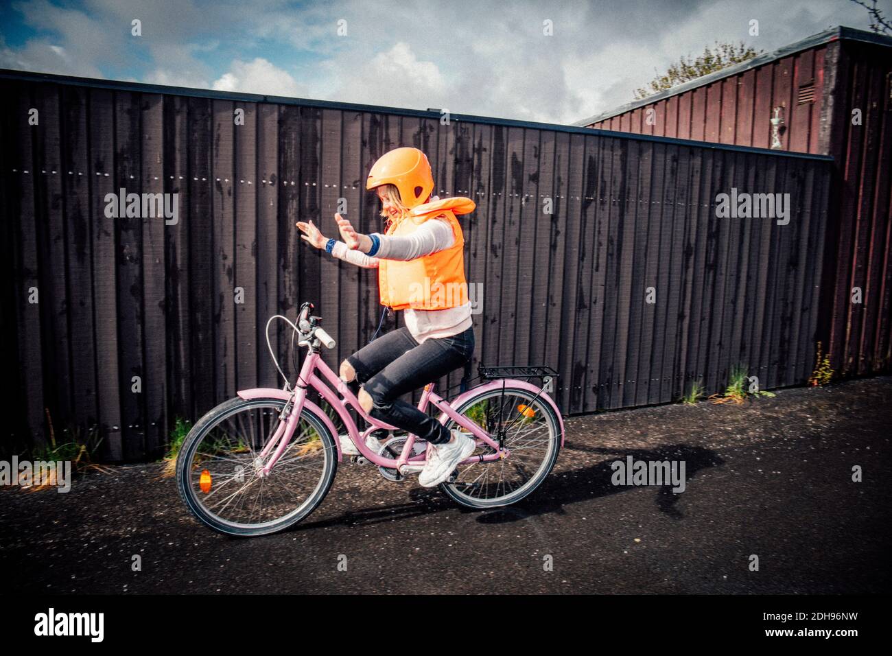 Ragazza sorridente che corre in bicicletta con le braccia distese su strada Foto Stock