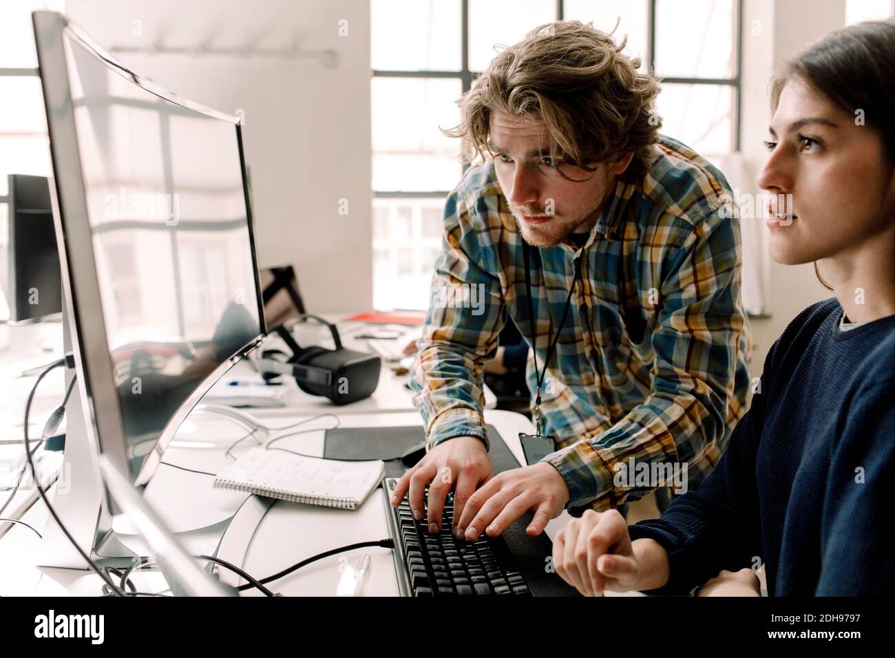 Uomo d'affari che scrive mentre il collega osserva il calcolatore in ufficio Foto Stock