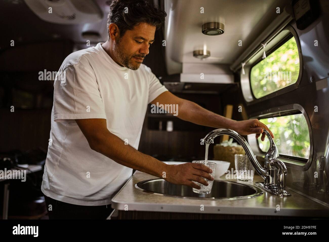 Uomo che riempie l'acqua potabile attraverso il rubinetto in camper rimorchio Foto Stock