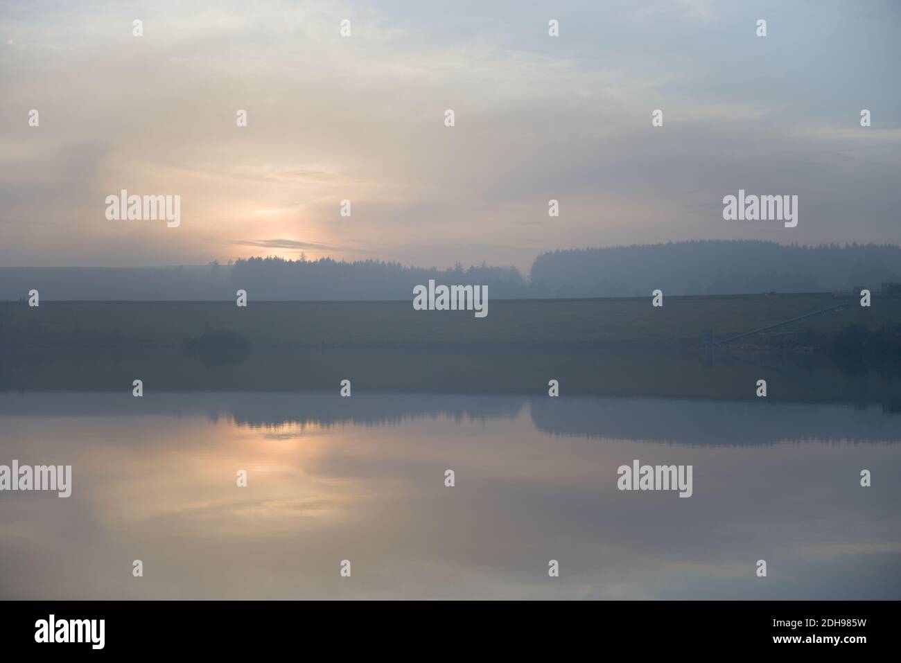 La calma dell'acqua del serbatoio riflette il tramonto appannato. Immagine orizzontale serena con colori pastello blu e arancione. Atmosfera frizzante con nuvole sgargianti Foto Stock
