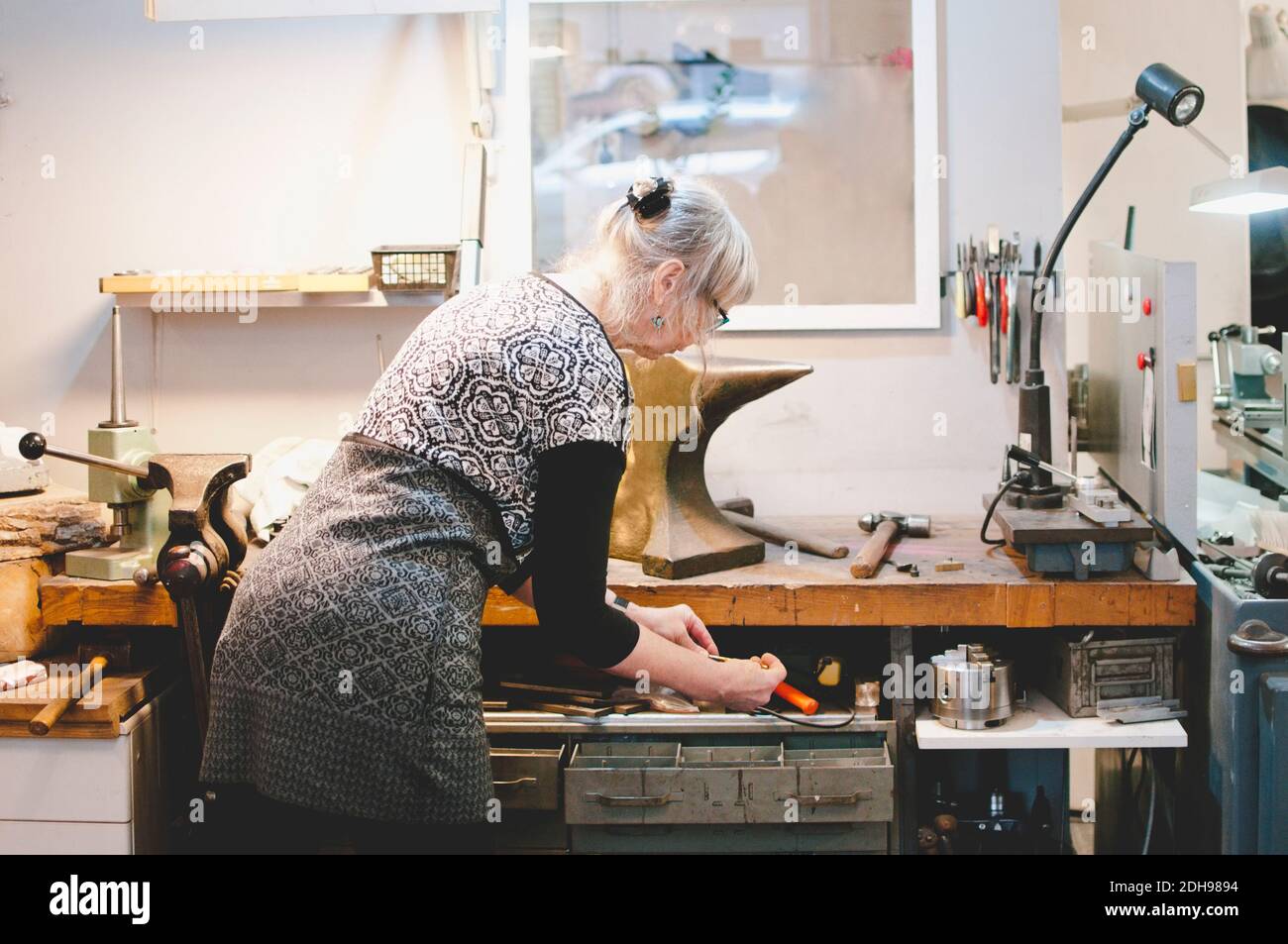 Vista posteriore della donna anziana che tiene la punta in officina Foto Stock