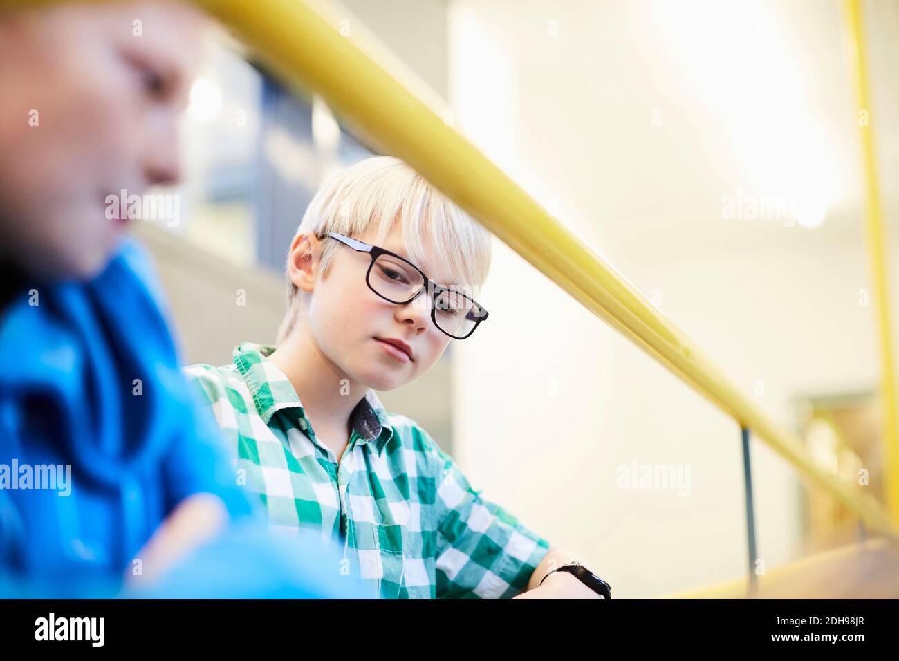Ragazzo seduto da un amico su una scala nella scuola media Foto Stock