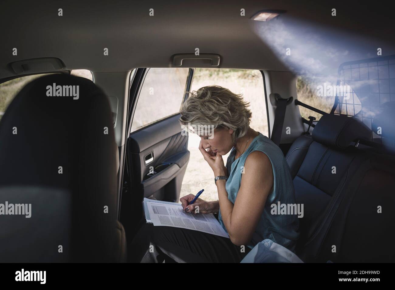 Vista laterale di una donna d'affari che scrive su un'automobile di documenti Foto Stock