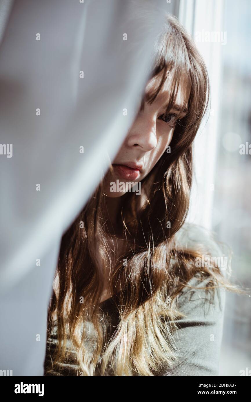 Ritratto di donna che si nasconde dietro la tenda della finestra Foto Stock