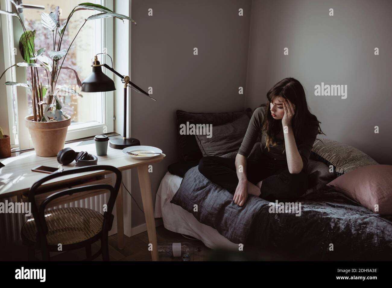 Donna depressa seduta sul letto a casa Foto Stock