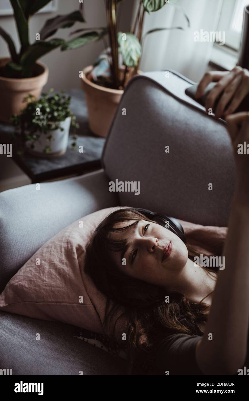 Donna sorridente che prende selfie mentre si sdraia sul divano a casa Foto Stock