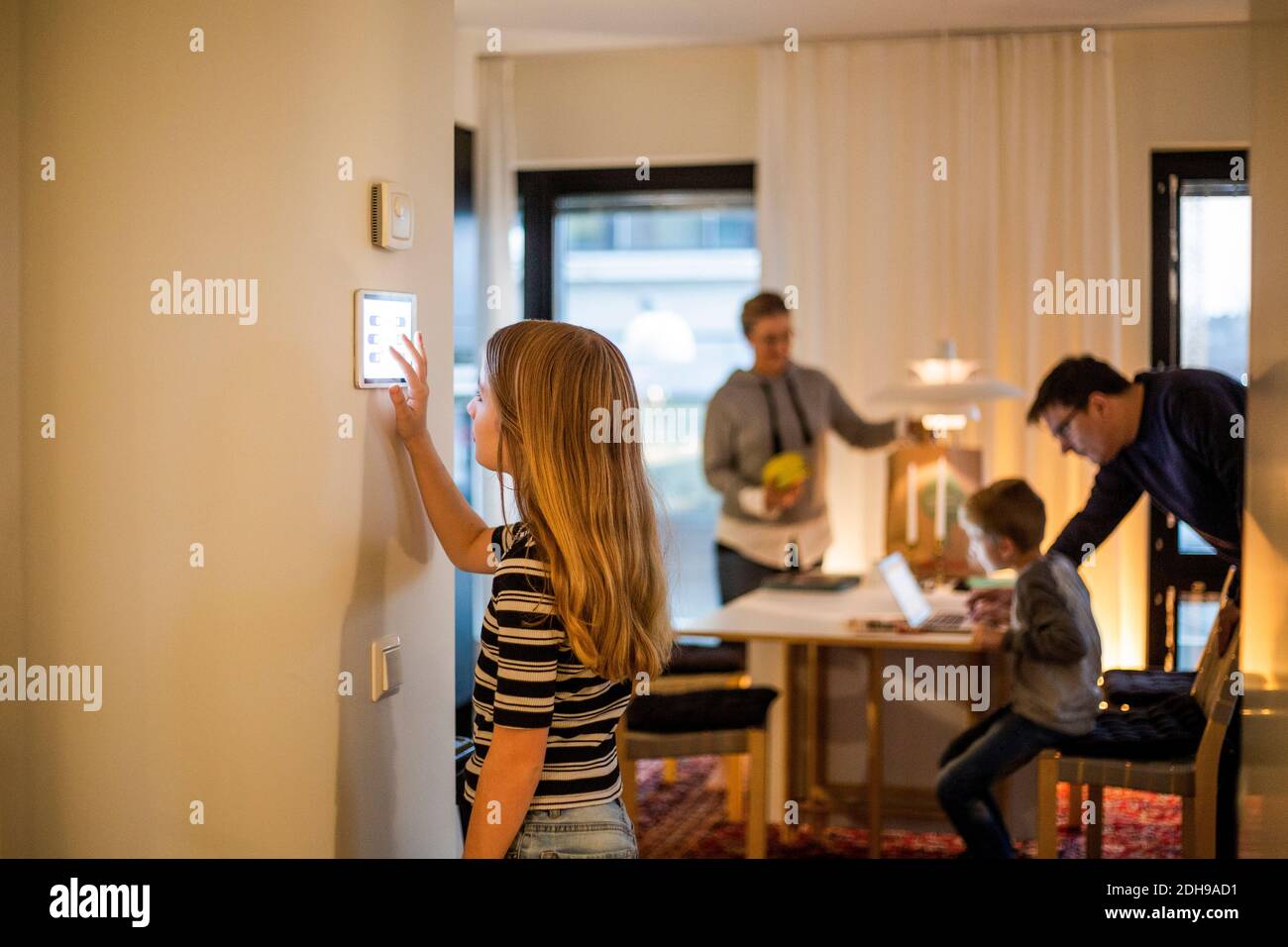 Ragazza che usa un tablet digitale sulla parete con la famiglia in background a casa intelligente Foto Stock