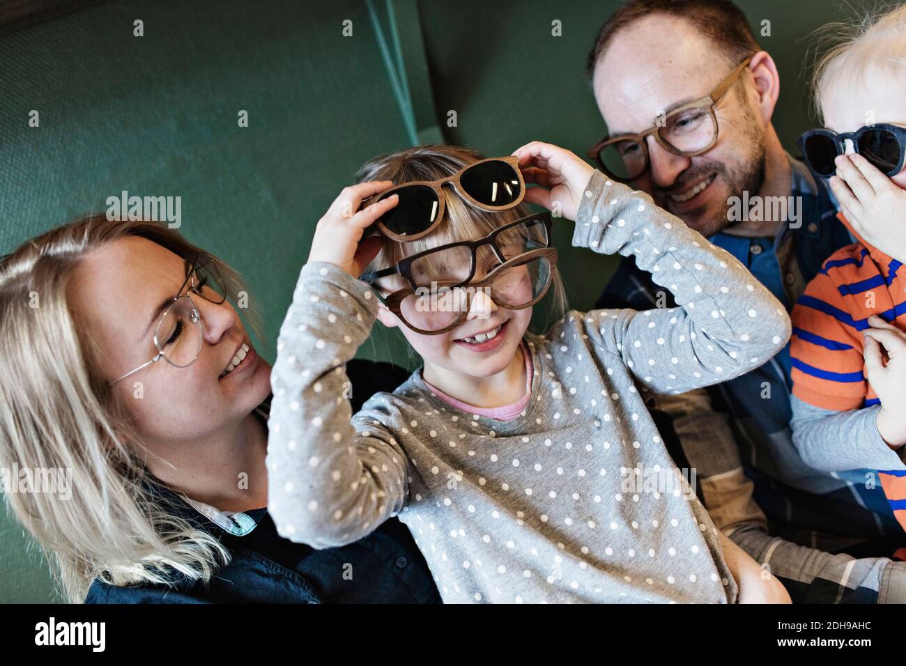 Famiglia felice che guarda la ragazza che indossa vari occhiali sul viso in officina Foto Stock
