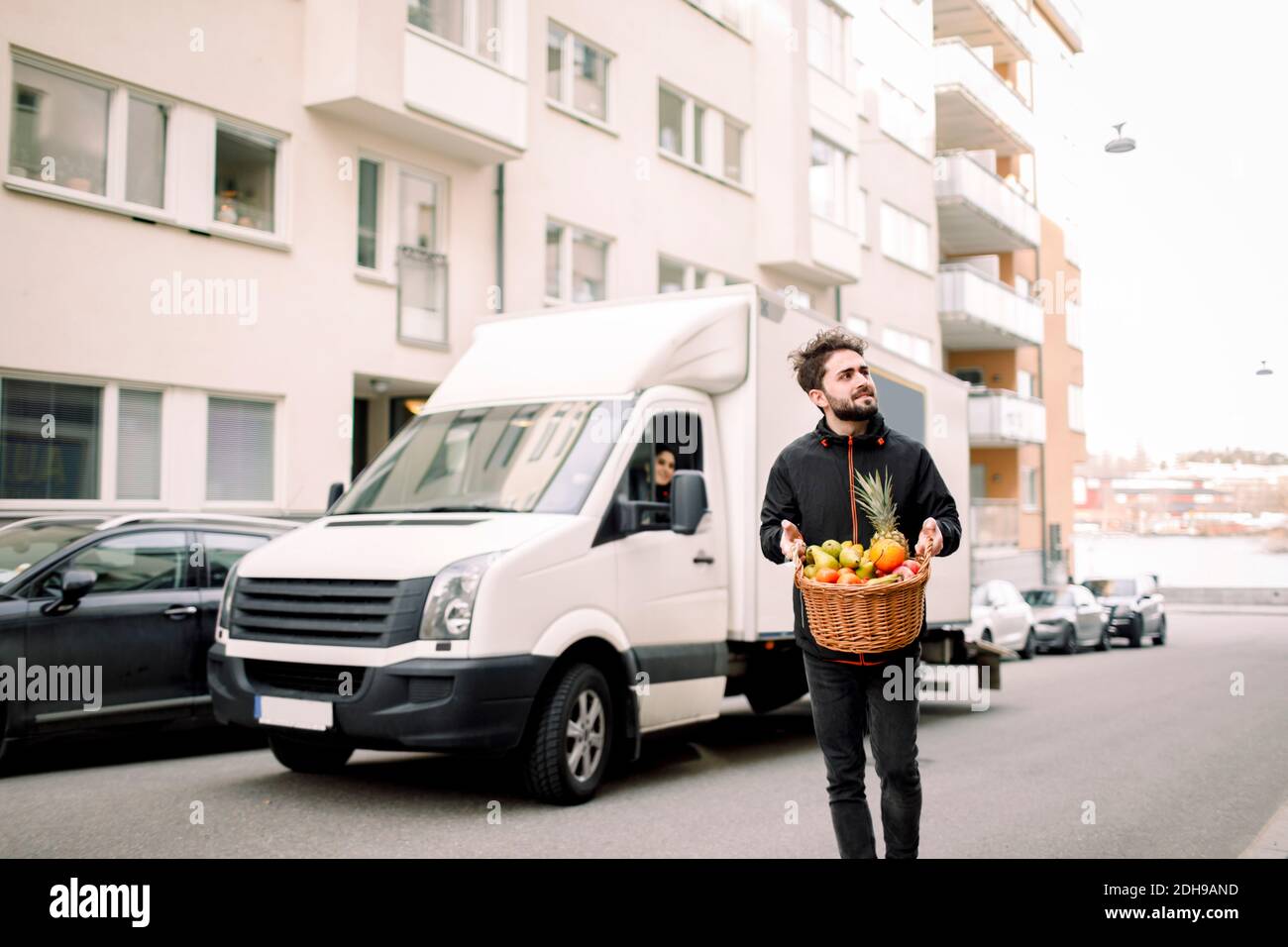 Giovane addetto alla consegna che porta un cestino di frutta sulla strada in città Foto Stock