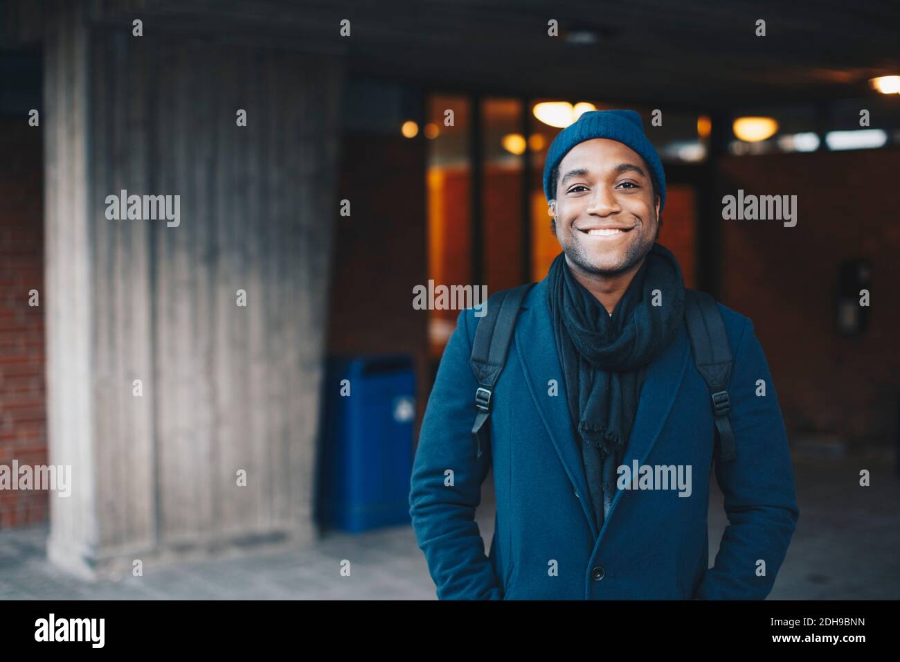 Ritratto di uomo felice che indossa abiti caldi blu e maglia cappello in piedi nel campus Foto Stock