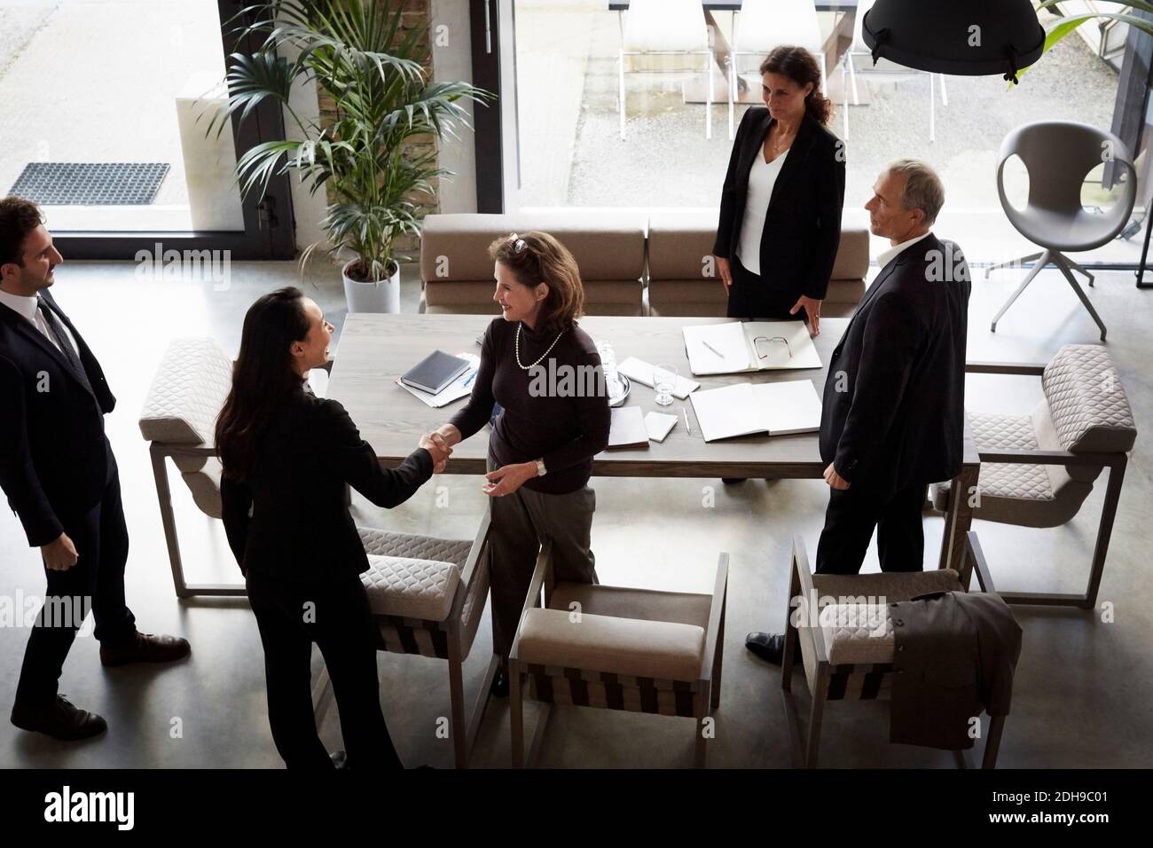 Vista ad alto angolo di donna consulente finanziario saluto businesswoman mentre colleghi in carica durante la riunione Foto Stock