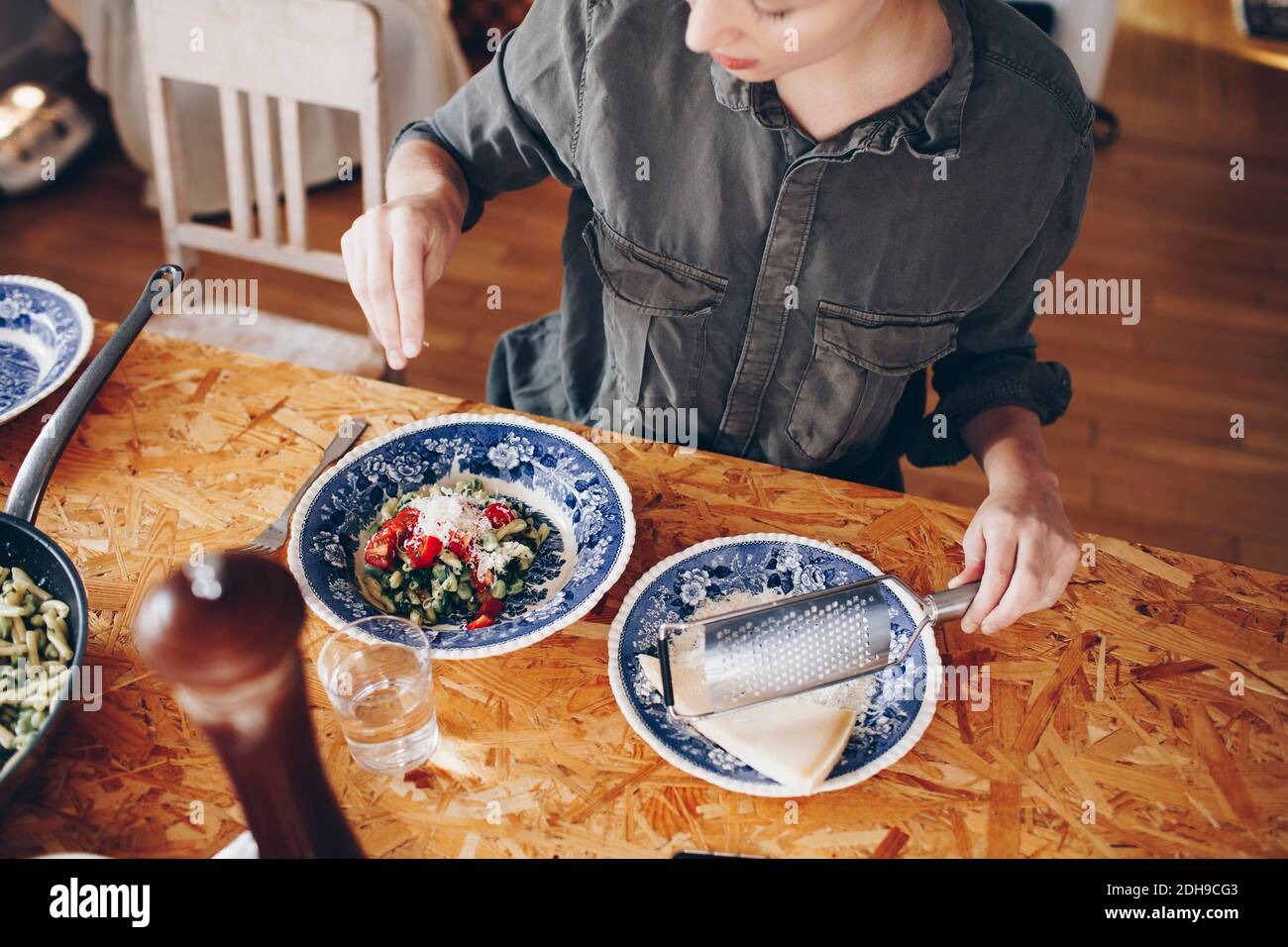 Vista ad alto angolo del formaggio da donna che spruzzava sulla pasta piatto a casa Foto Stock