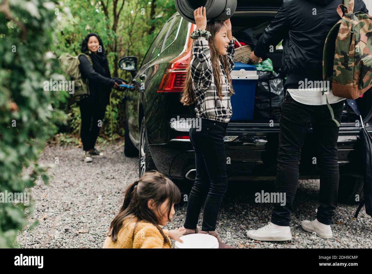 Figlia con i genitori che caricano i bagagli nel bagagliaio dell'auto elettrica Foto Stock