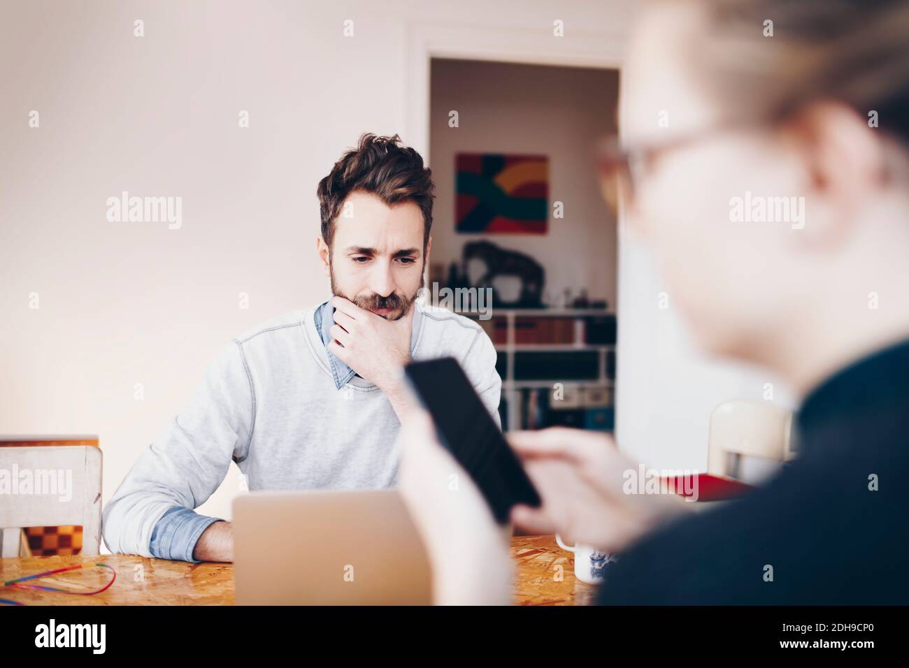 Uomo che lavora su un computer portatile mentre la donna usa il telefono cellulare a. casa Foto Stock