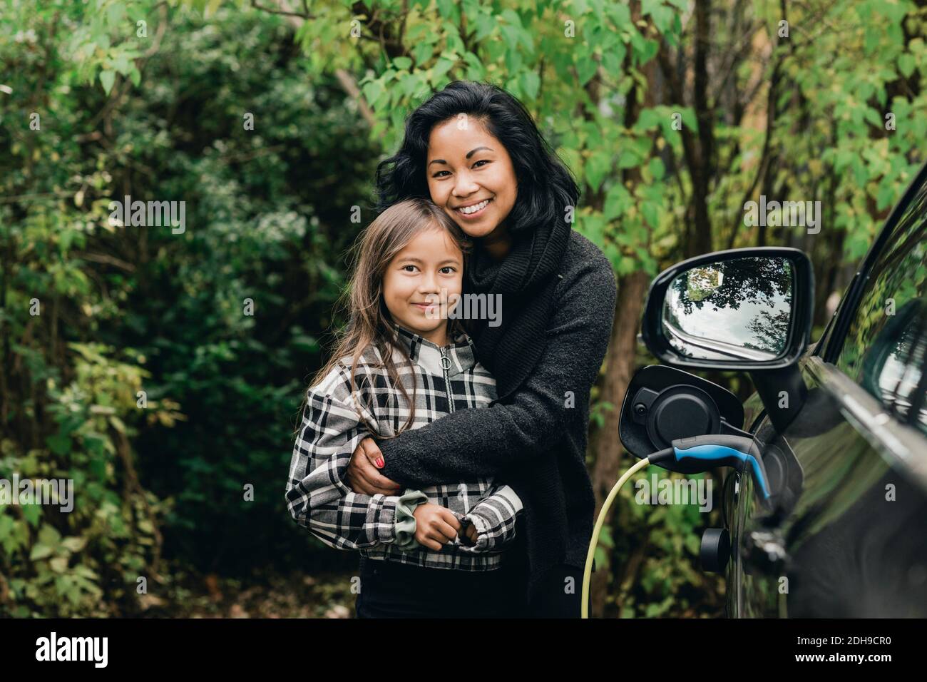 Ritratto di donna mid adulta con figlia in auto elettrica sulla stazione di ricarica Foto Stock