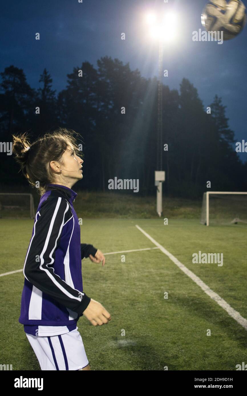 Vista laterale della ragazza che gioca con la palla di calcio sul campo contro gli alberi Foto Stock