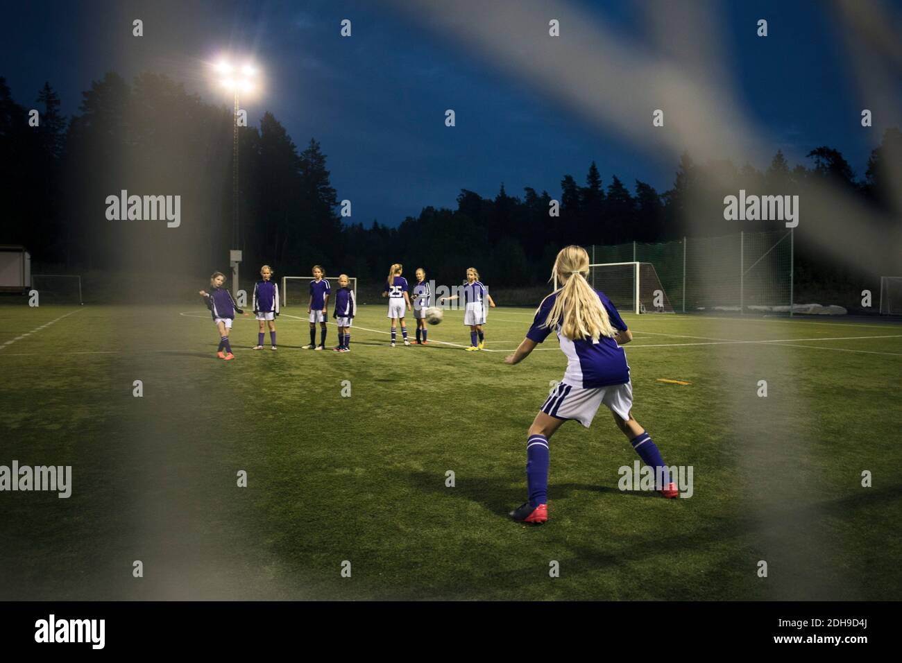 Ragazze che giocano a calcio visto da gol post rete sul campo contro il cielo Foto Stock