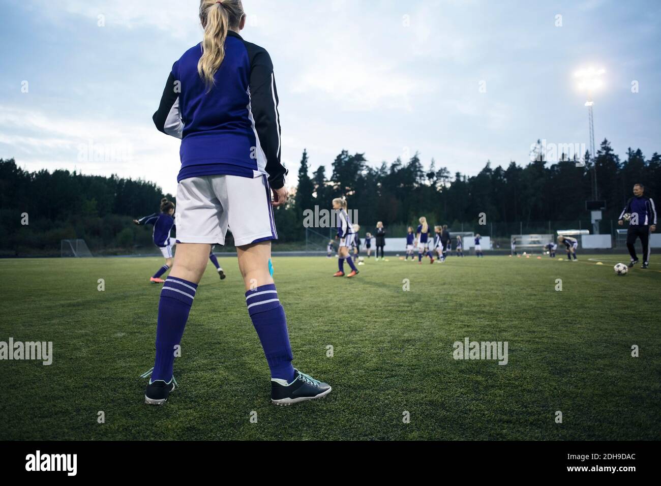 Vista posteriore della ragazza che guarda i giocatori che giocano sul calcio campo Foto Stock