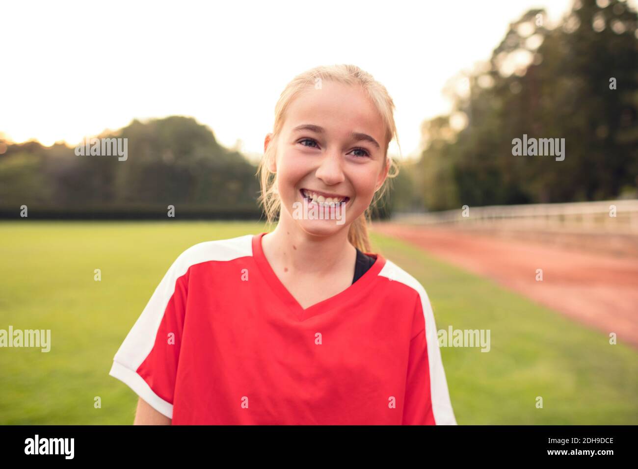 Ragazza felice che indossa uniforme sportiva rossa in piedi sul campo di calcio contro il cielo Foto Stock