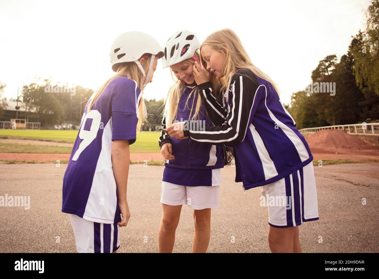 Felici giocatori di calcio femminile che cercano nel telefono cellulare in piedi sentiero da campo di calcio Foto Stock