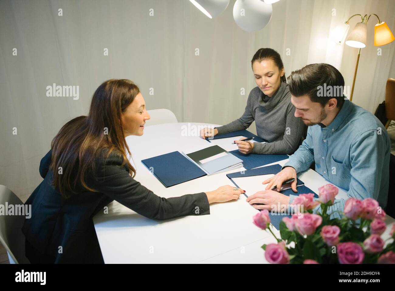 Vista ad alto angolo dell'agente immobiliare femminile maturo che assiste giovane coppia con brochure alla scrivania in ufficio Foto Stock