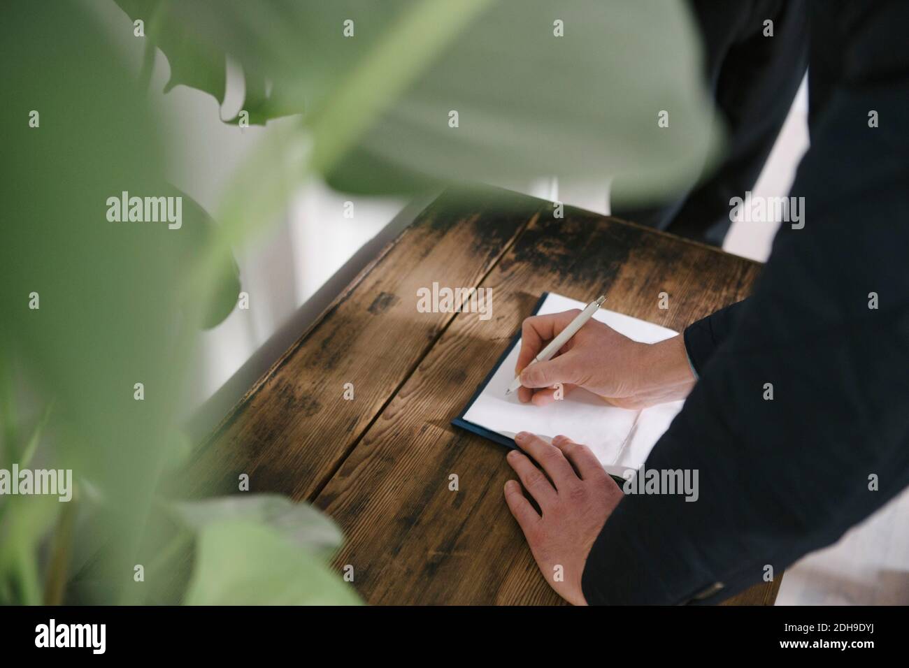 Visualizzazione ad alto angolo della scrittura di un uomo sul documento a casa Foto Stock