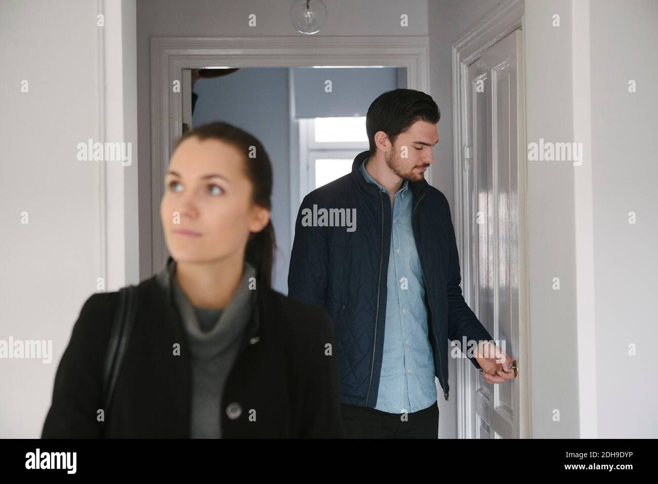 Giovane uomo che guarda la porta mentre si è in piedi con la donna dentro corridoio Foto Stock