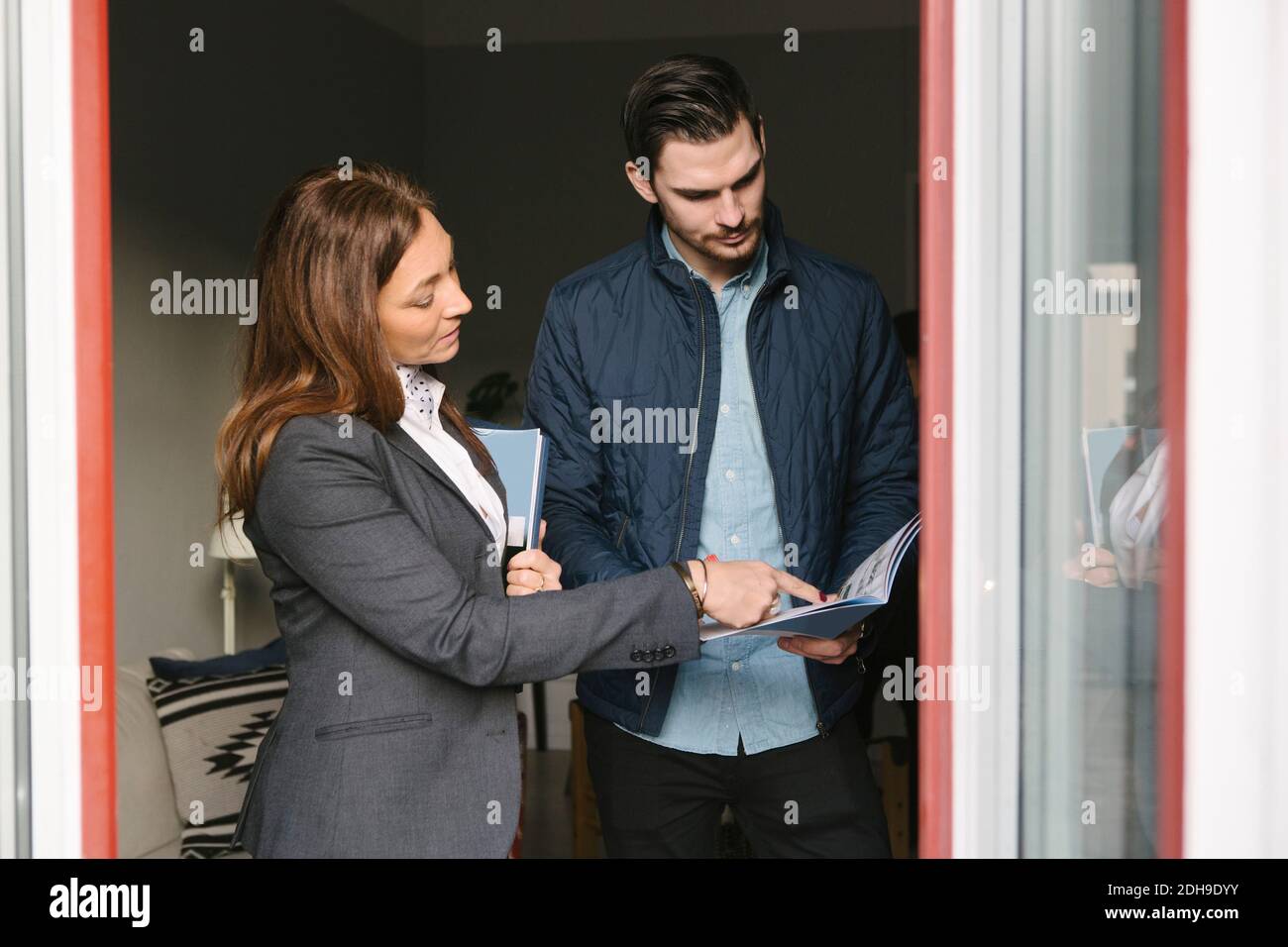 Il realtor femminile assiste l'uomo mentre punta alla brochure dalla finestra Foto Stock