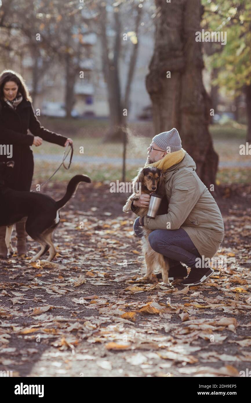 Tutta la lunghezza dell'uomo accovacciato mentre abbracciando il cane da donna con animali domestici al parco Foto Stock