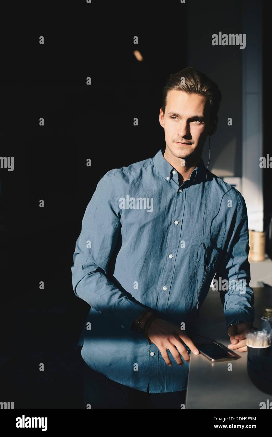 Uomo d'affari premuroso in piedi con smartphone al tavolo in modo brillante ufficio illuminato Foto Stock