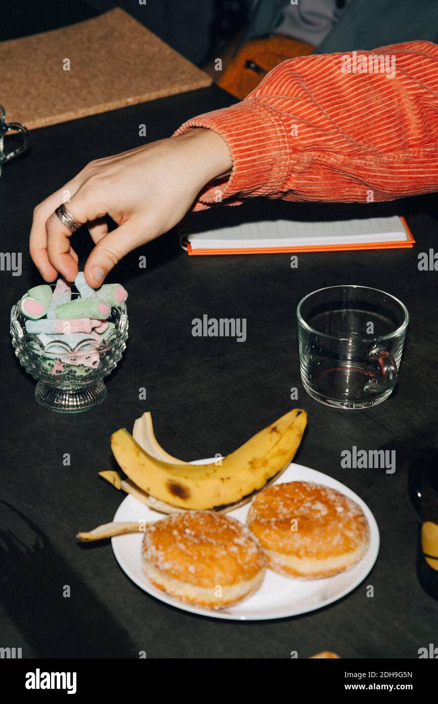 Mano tagliata di uomo che mangia caramelle a tavola in ufficio Foto Stock