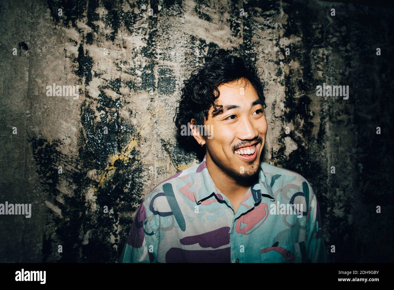 Imprenditore sorridente che guarda via mentre si sta contro il muro in creativo ufficio Foto Stock