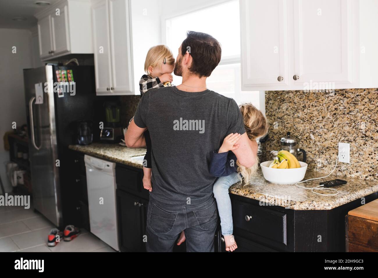 Vista posteriore del padre che si prende cura delle figlie in cucina a casa Foto Stock