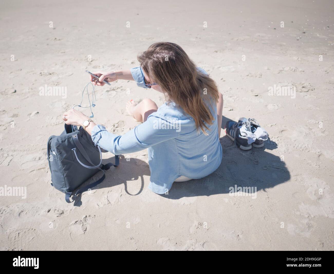 Vista ad alto angolo della donna con telefono cellulare mentre si prende auricolari fuori dalla borsa in spiaggia Foto Stock