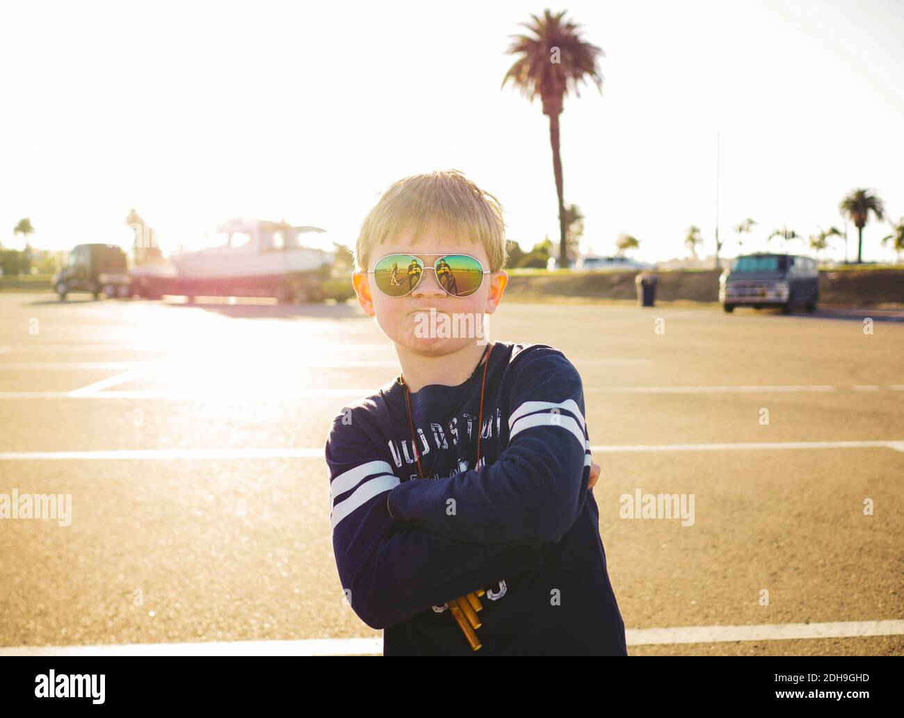 Ritratto di ragazzo sicuro che indossa occhiali da sole mentre in piedi le braccia incrociate al parcheggio durante il giorno di sole Foto Stock