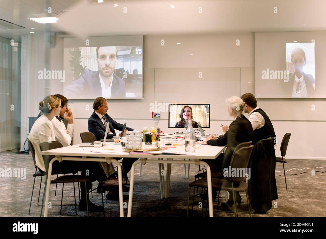 Professionisti maschili e femminili che discutono nell'incontro d'affari globale visto attraverso la parete di vetro sul luogo di lavoro Foto Stock
