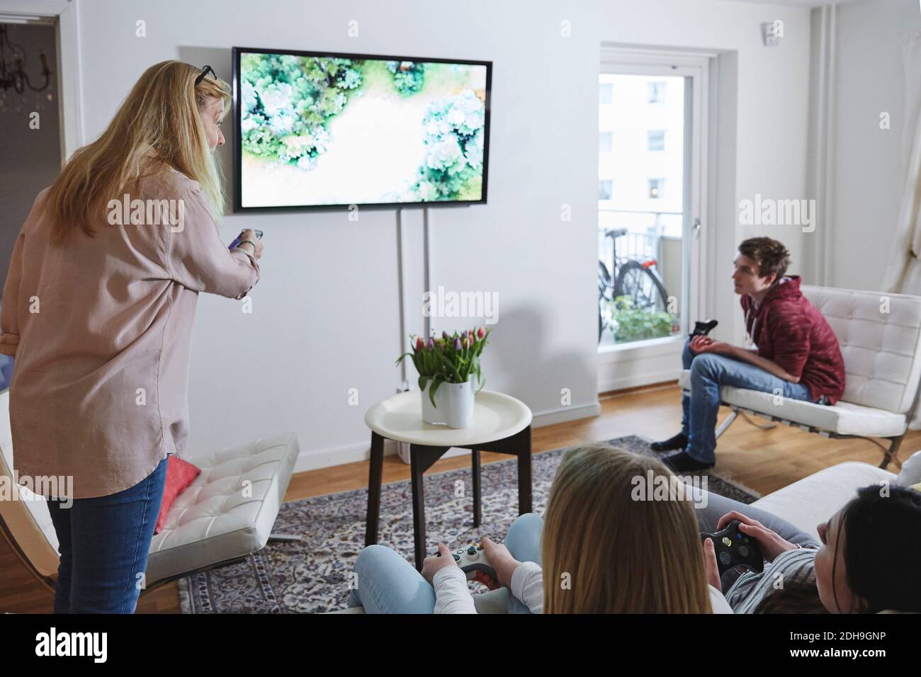 Madre con telecomando che guarda i bambini che giocano ai videogiochi in soggiorno Foto Stock