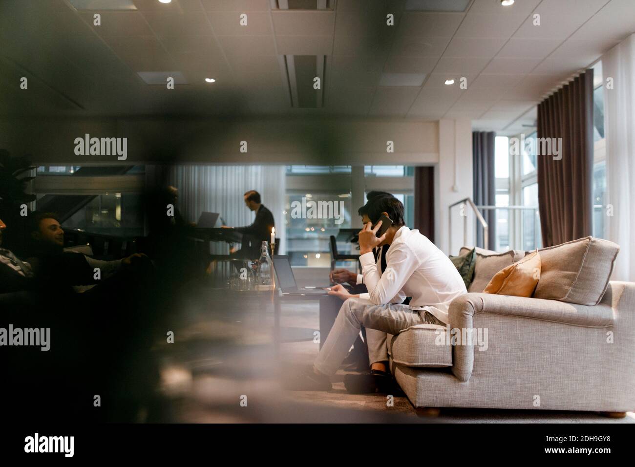 Uomo d'affari che parla sul telefono cellulare mentre si siede con i colleghi riunione durante la conferenza globale in ufficio Foto Stock