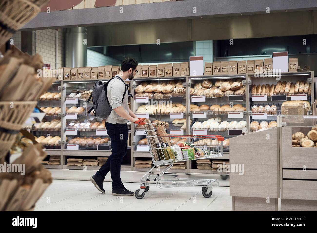 Vista laterale dell'uomo che cammina con il carrello mentre si guarda pane nel supermercato Foto Stock