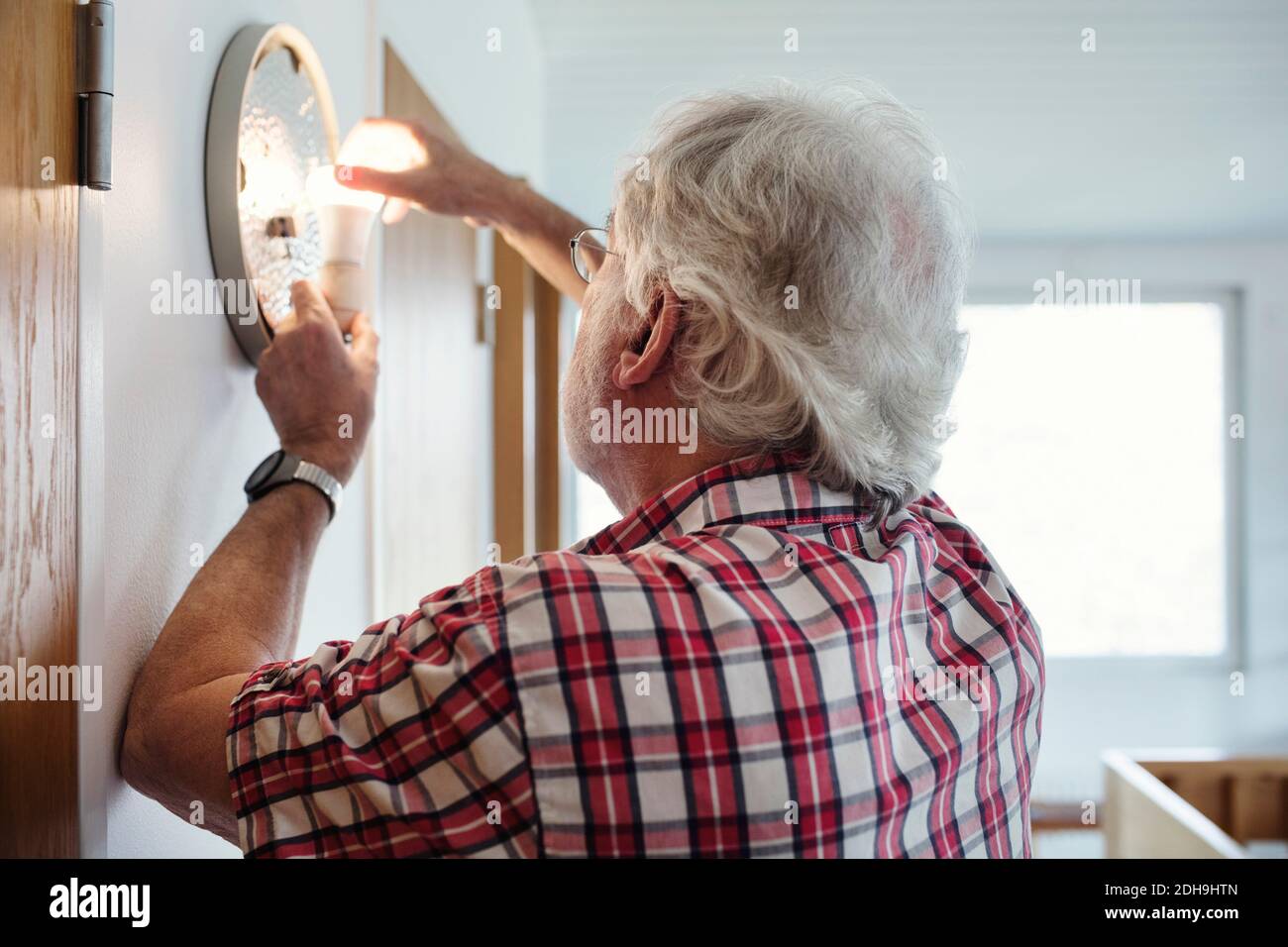 Uomo anziano che cambia lampadina in conce a casa Foto Stock