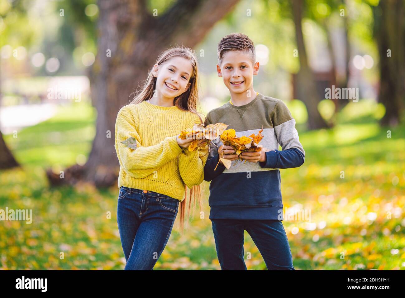Felici gemelli adolescenti ragazzo e ragazza che si abbracciano l'un l'altro in autunno parco che tiene caduto foglie gialle in mano sole weathe Foto Stock