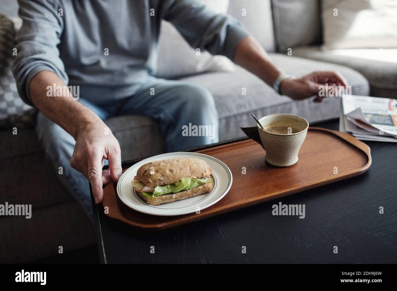 Sezione centrale dell'uomo anziano con panino e tazza seduti sopra divano a casa Foto Stock