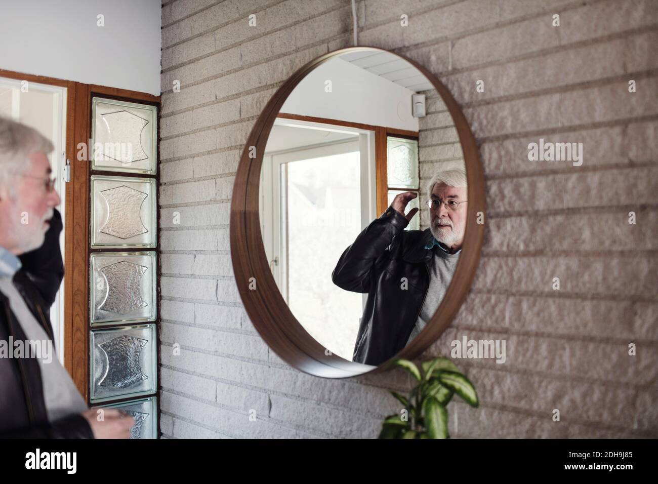 Uomo anziano che guarda lo specchio mentre si trova in camera Foto Stock