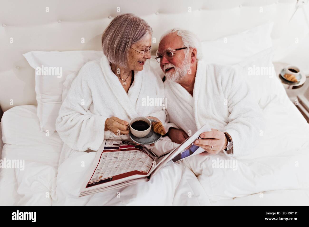 Donna anziana che guarda l'uomo che tiene il giornale mentre ha il caffè a letto in hotel Foto Stock