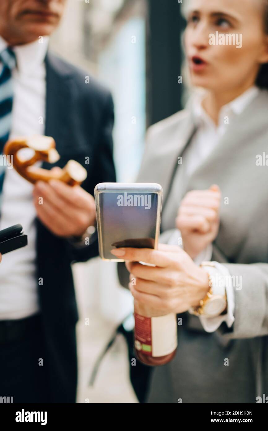 Persona di affari femminile con il telefono intelligente che parla con il collega maschio in città Foto Stock