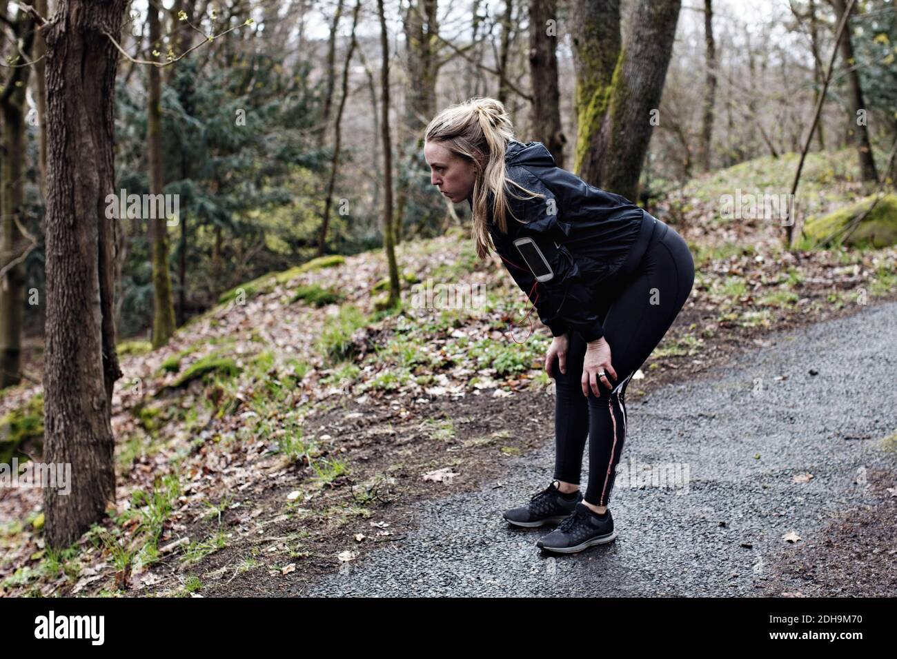 Tutta la lunghezza dell'atleta stanca in piedi con le mani ginocchia nella foresta Foto Stock